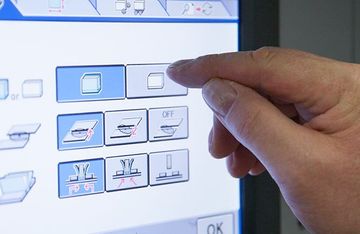 Finger in Großaufnahme bedient digitales Bedienfeld einer Druckmaschine