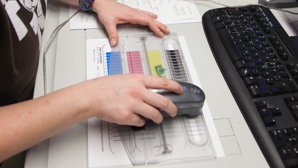 Hand mit Densitometer auf Farbkarte bei der Kalibrierung 